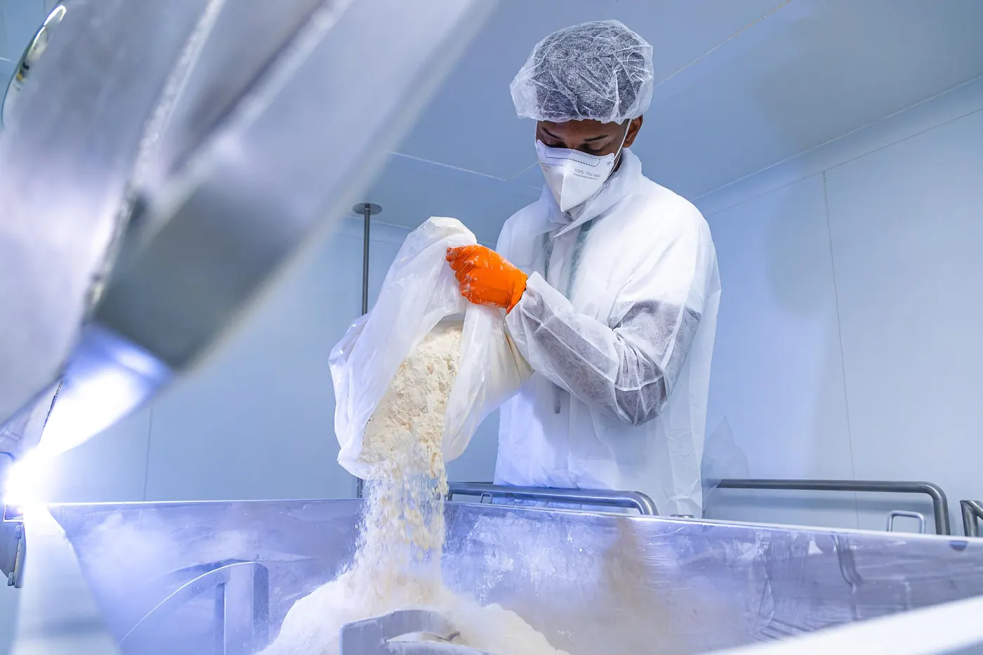 Operatore in camice e mascherina versa polvere nutraceutica in un miscelatore industriale in acciaio