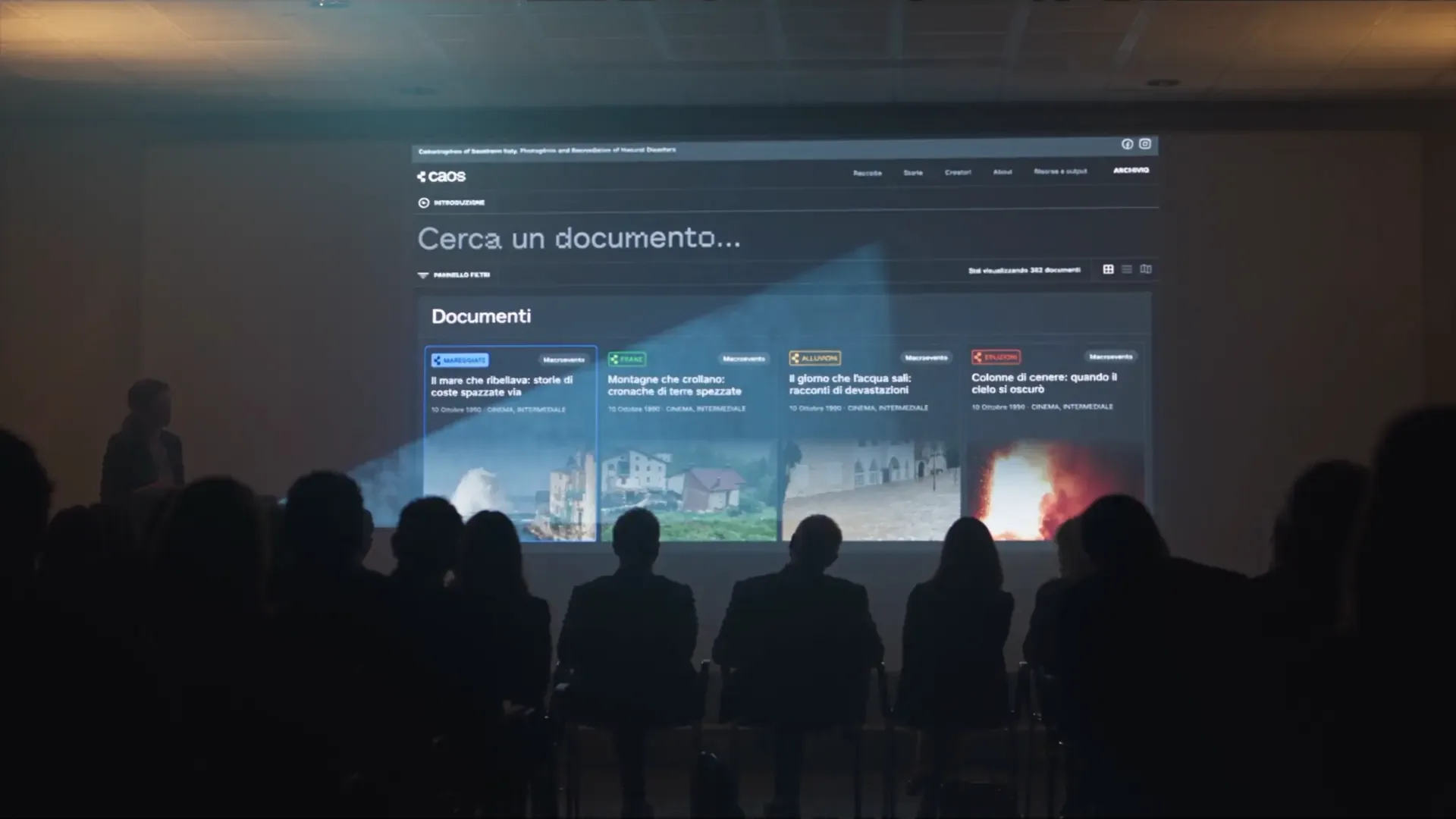 L'archivio digitale di caos proiettato su un grande schermo durante una conferenza, con il pubblico in penombra in primo piano